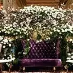 photo booth set up for a wedding. Purple velet chari with lots of flower above it and two sitting chairs on each side.
