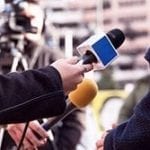 stock image of a reporters holding microphones pointed a person you cannot fully see