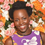African American lady smiling in front of a wall of multi colored roses