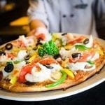 chef holding a fully cooked pizza with vegetables on it