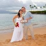 a newly married couple on the beach in Maui holding a signed that says just got Maui'd