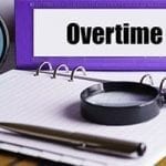 stock image of purple binder with the word 'overtime' written on it. There is a clock, pin and magnifying glass on the table as well