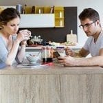 stock image of a Caucasian man and women having breakfast a table looking at technology