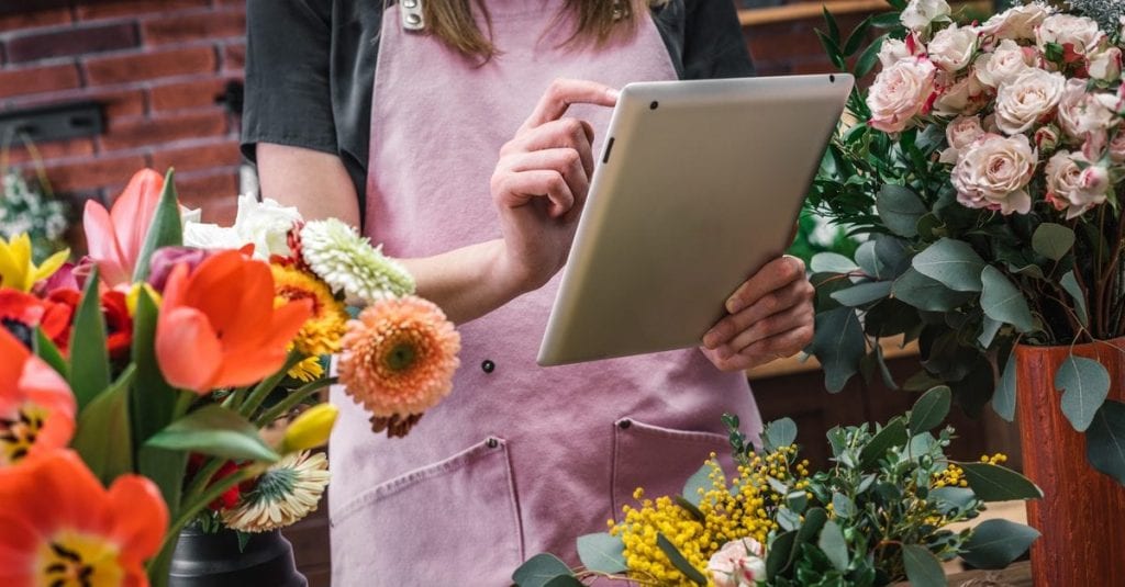 female working in a flower shop writing on an ipad