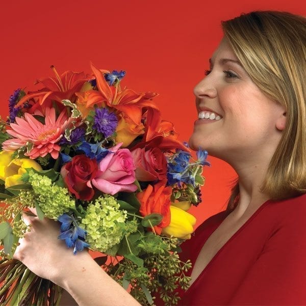 Middle aged asian female smelling a flower arrangement, smiling.